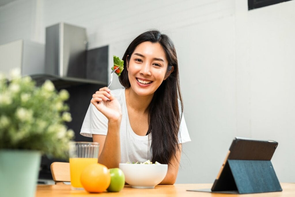 Mulher sorrindo segurando um garfo com salada