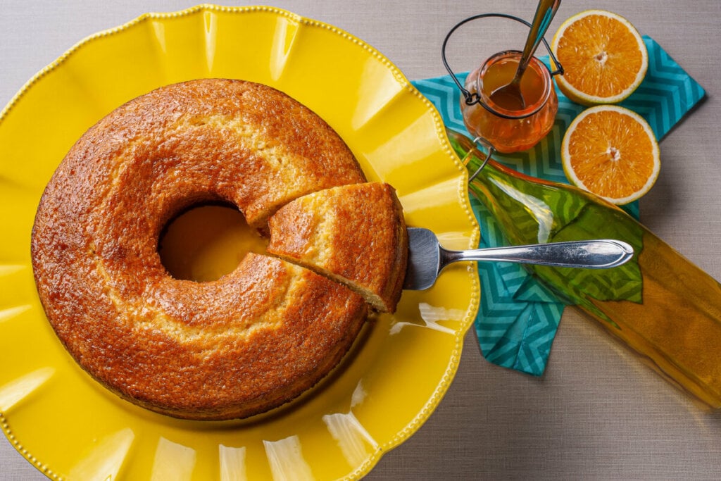 Bolo de laranja em cima de um recipiente amarelo com um pedaço sendo cortado por uma espátula