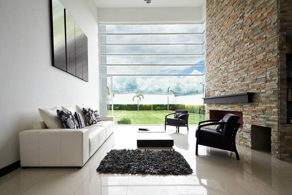 Sala de estar com vista para o jardim, sofá banco e parede de pedras com mesa de centro preta