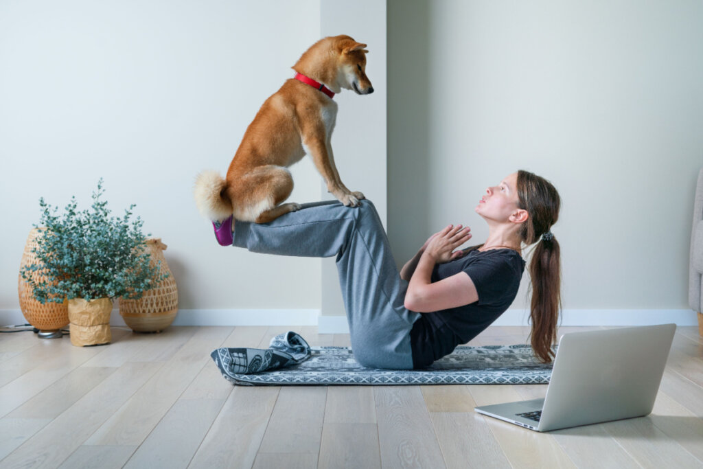 Jovem mulher em posição de ioga equilibrando com seu cachorro.