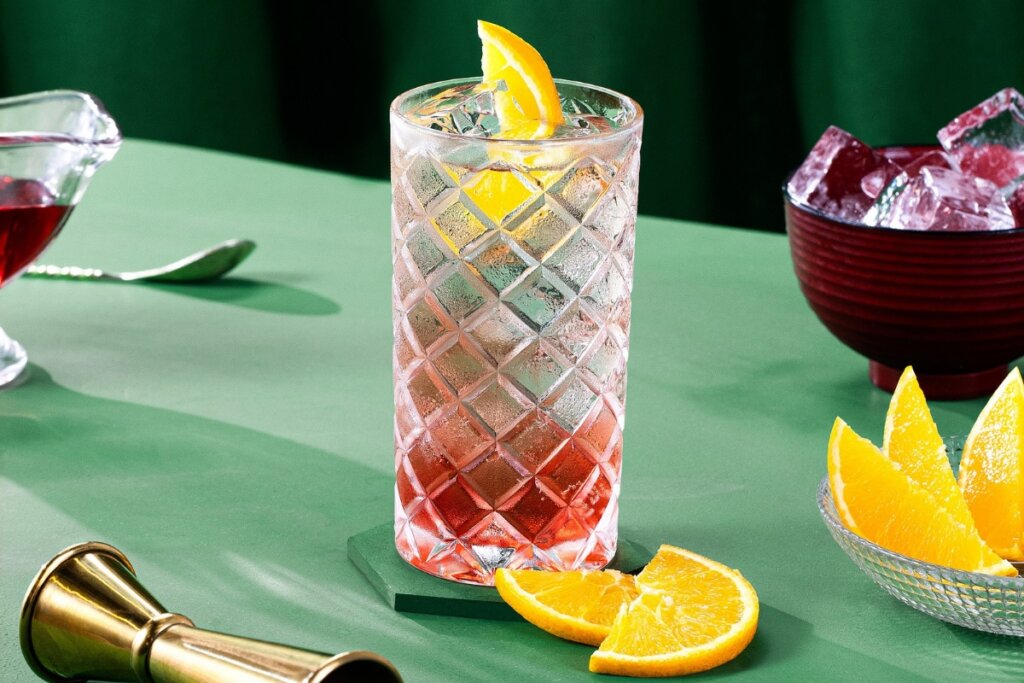 Copo de vidro com drink rosa decorado com rodelas de laranja 