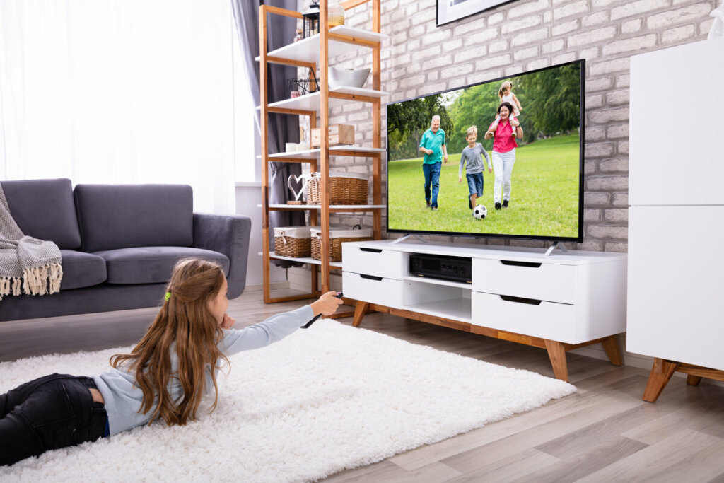 Menina deitada em um tapete branco assistindo à televisão 