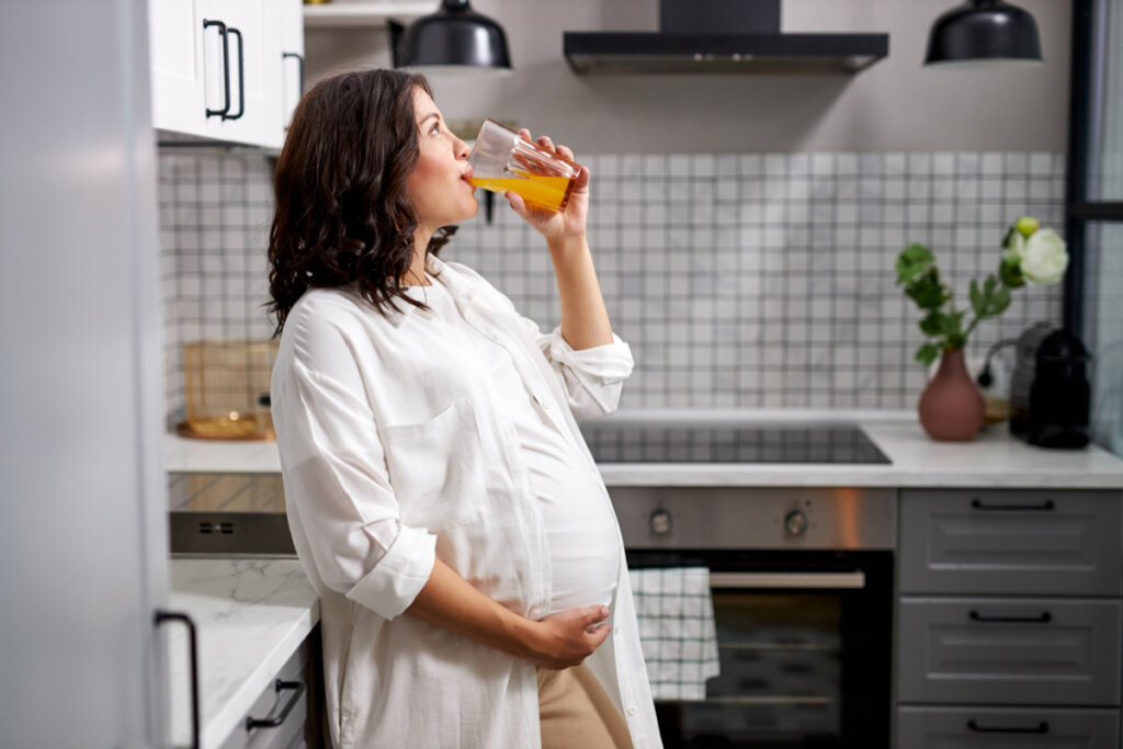 Mulher grávida tomando suco de laranja na cozinha de casa