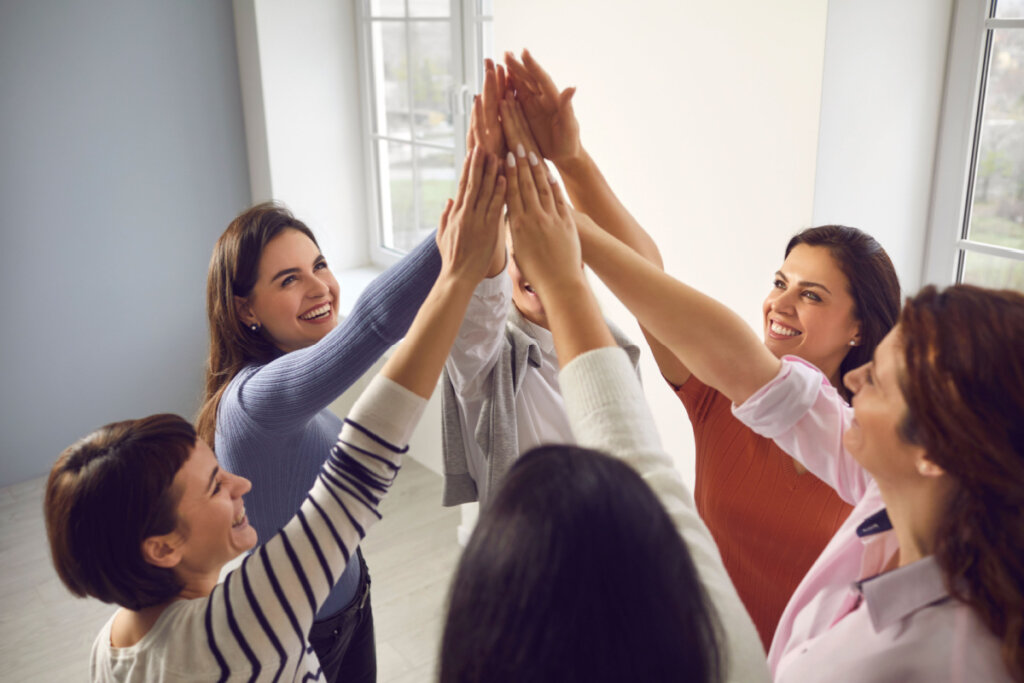 Equipe de mulheres sorridentes felizes e confiantes em pé em círculo e juntando as mãos, sentindo-se unidas e fortalecidas.