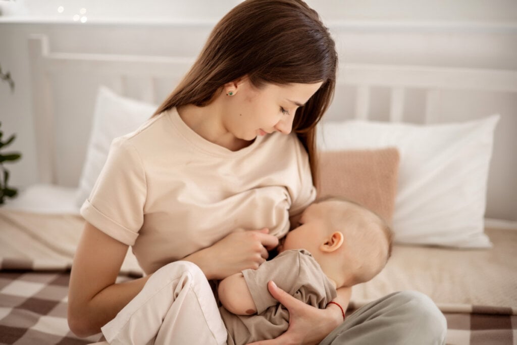 Mulher sentada na cama amamentando bebê