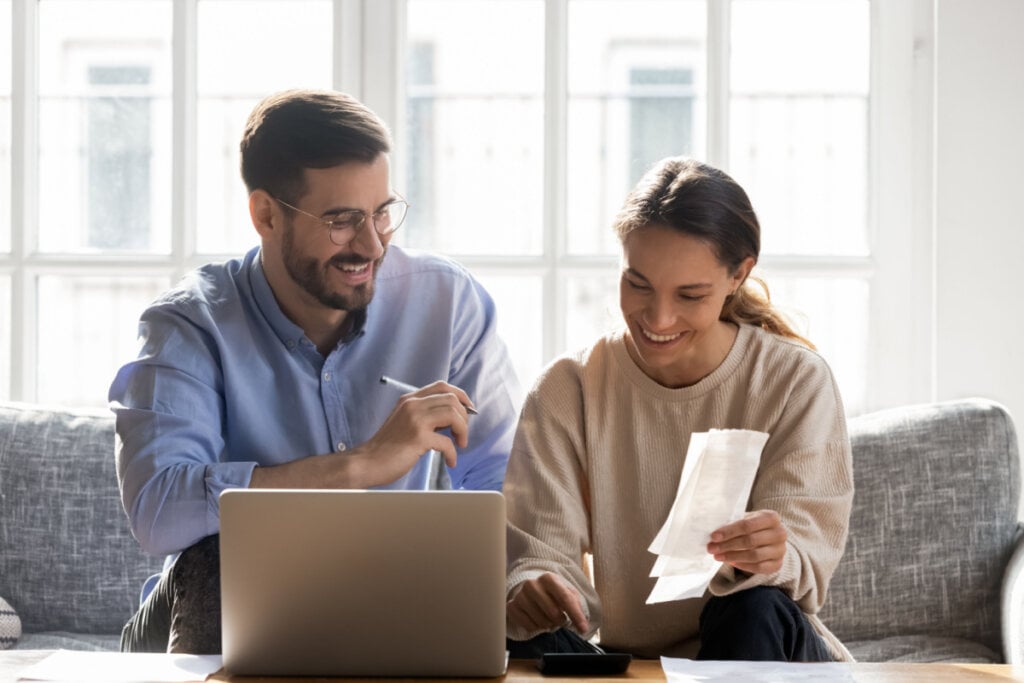 Homem e mulher sorridentes organizando vida financeira sentados em sofá da sala