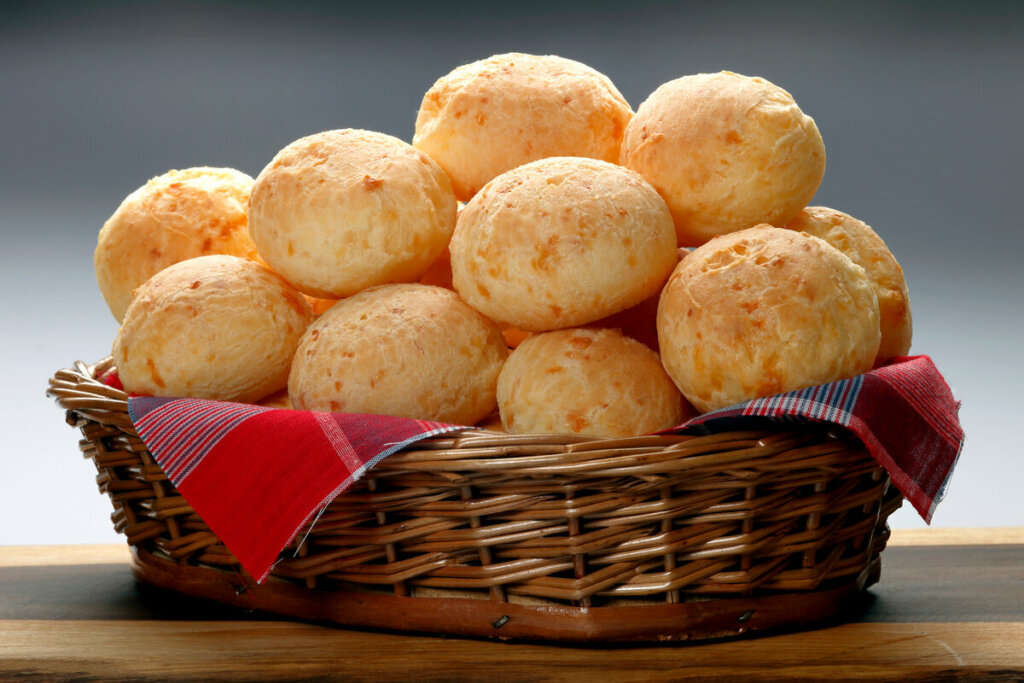 Pães de queijo empilhados dentro de uma cesta com pano vermelho