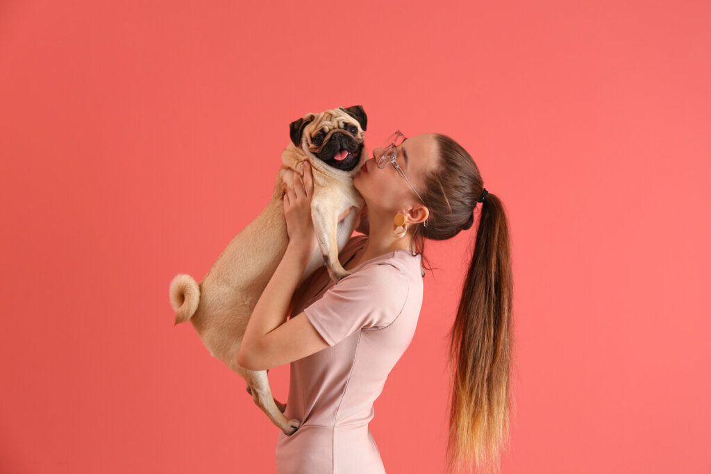 Mulher segurando um cachorro e o beijando em frente a um fundo rosa