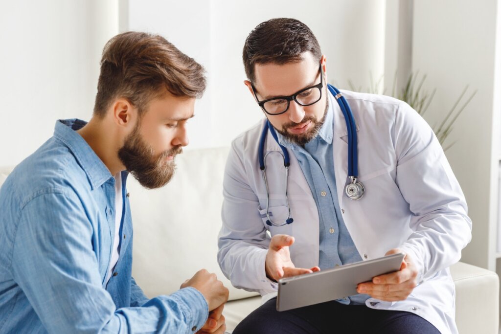 Homem e médico sentados conversando e olhando para a tela de um tablet