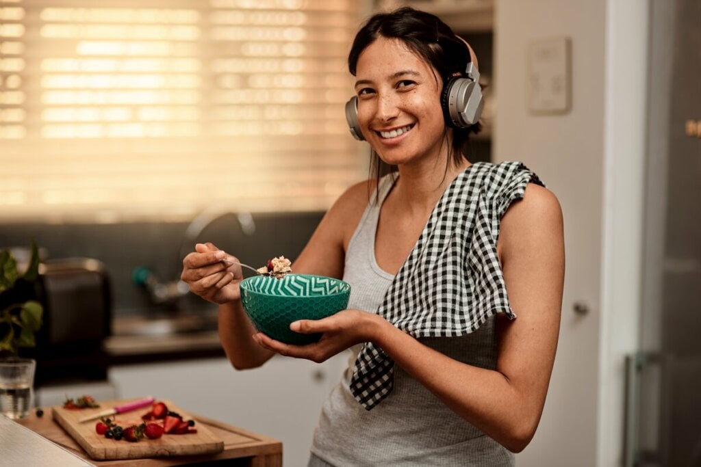 Mulher sorrindo usando fone de ouvido e segurando uma colher e uma tigela