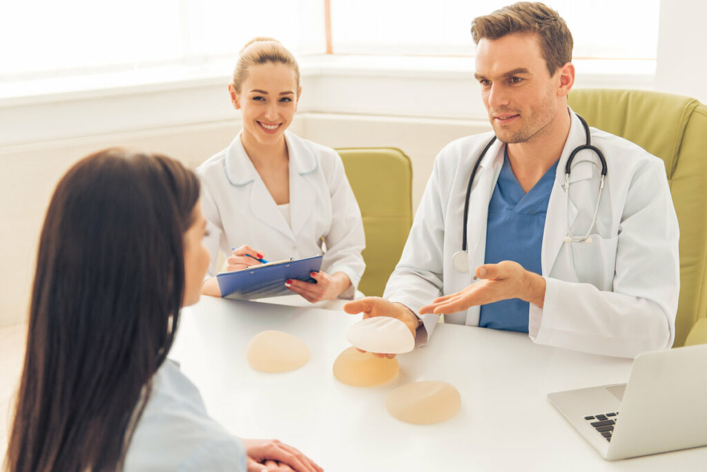 Mulher sentada conversando com dois médicos com próteses mamárias em cima de uma mesa branca 