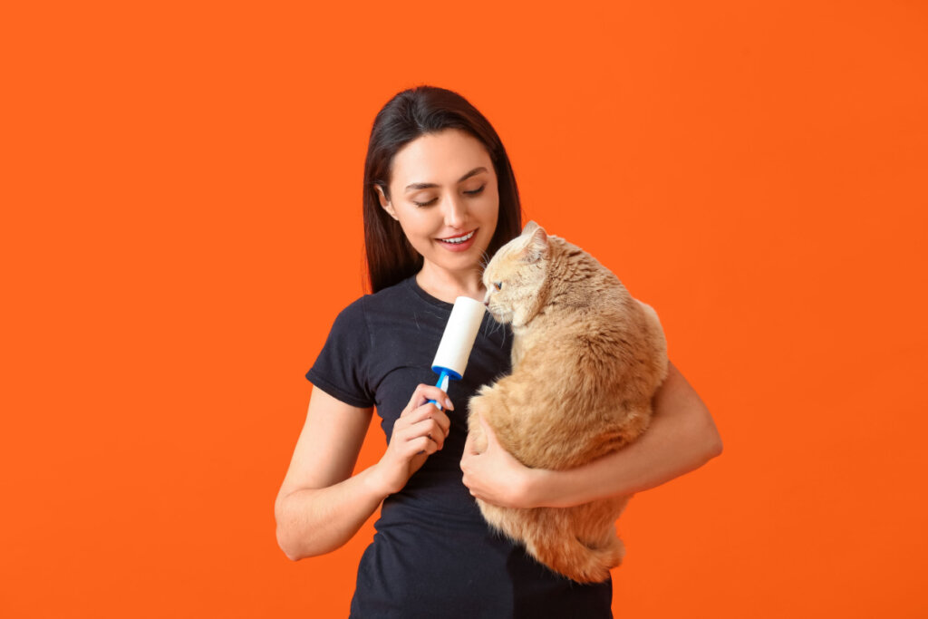 Mulher de roupa preta com gato laranja no colo e rolo para remoção de pelos