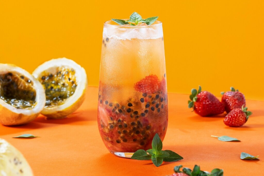 Copo de vidro com drink de maracujá e morango decorado com folhas de manjericão