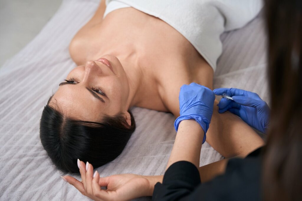 Mulher deitada com uma médica usando luvas fazendo procedimento estético em suas axilas