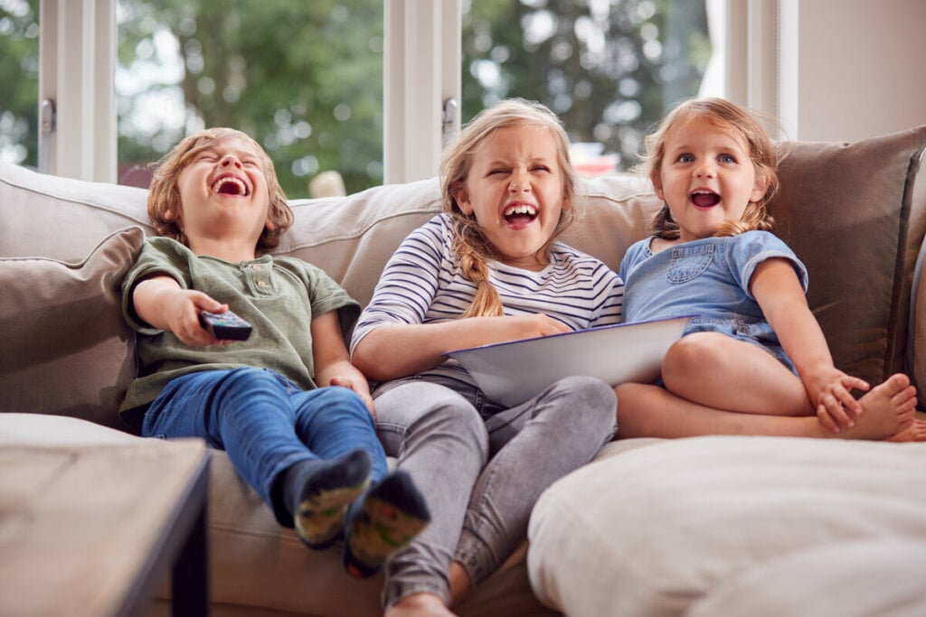 Duas meninas e um menino sentados em um sofá assistindo à televisão