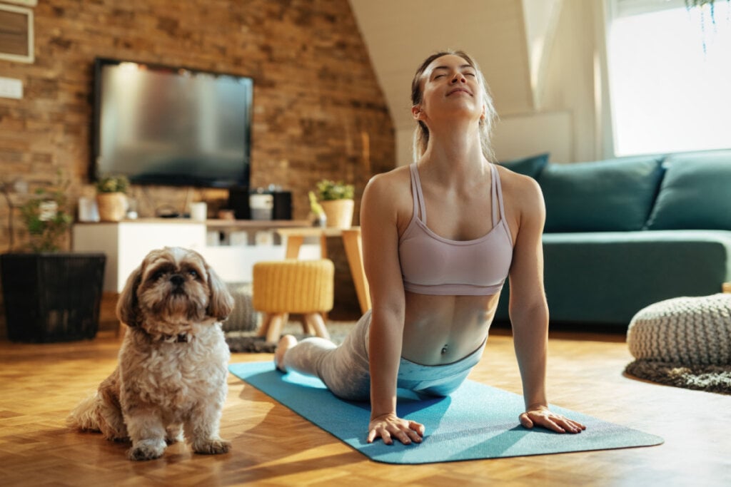Mulher em praticando Yoga com seu cachorro em casa.