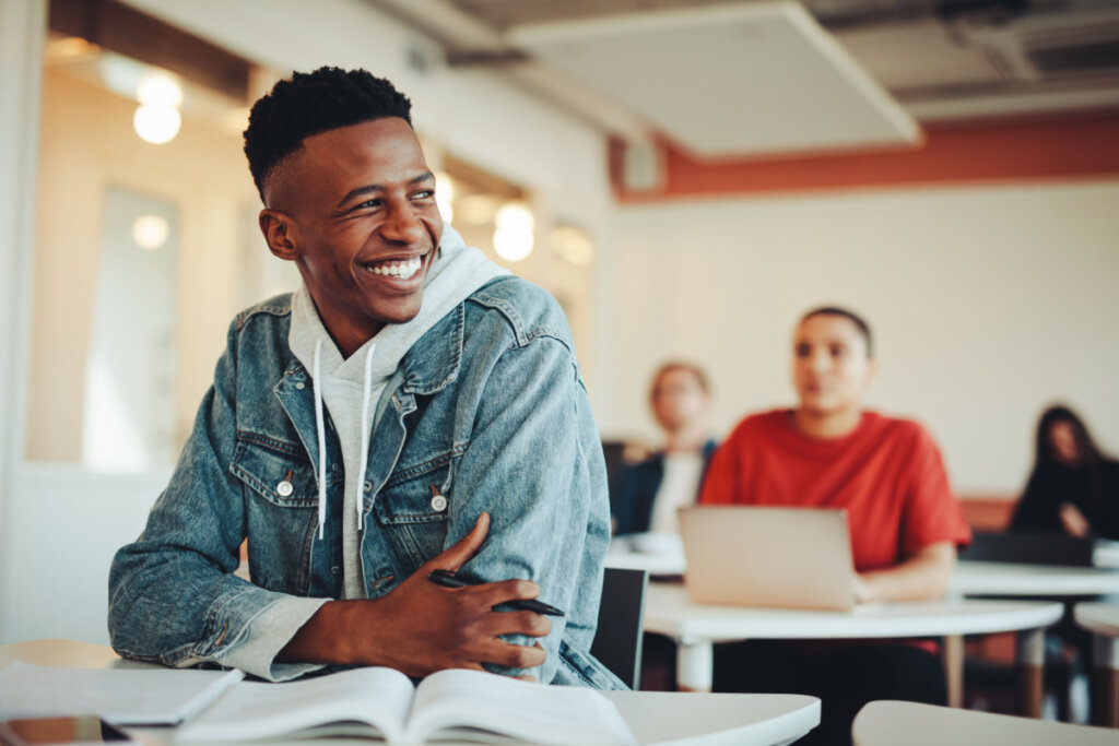 Estudante sentado na sala de aula da universidade olhando para longe e sorrindo