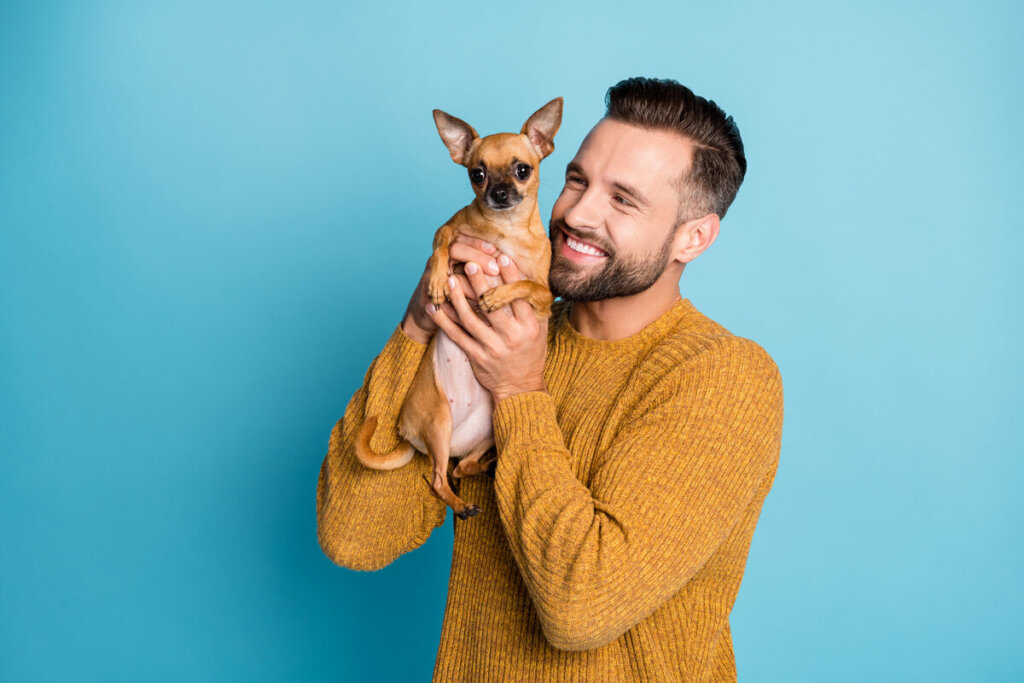 Homem vestindo blusa amarela segurando um cachorro e sorrindo
