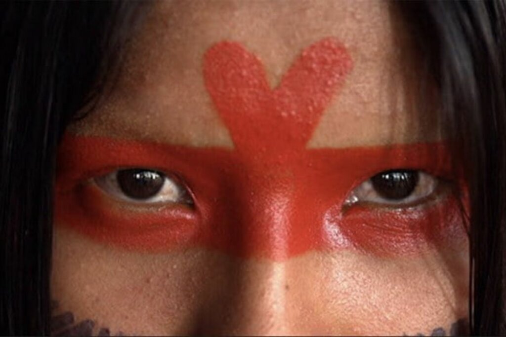 Mulher indígena com o rosto pintado olhando para foto 