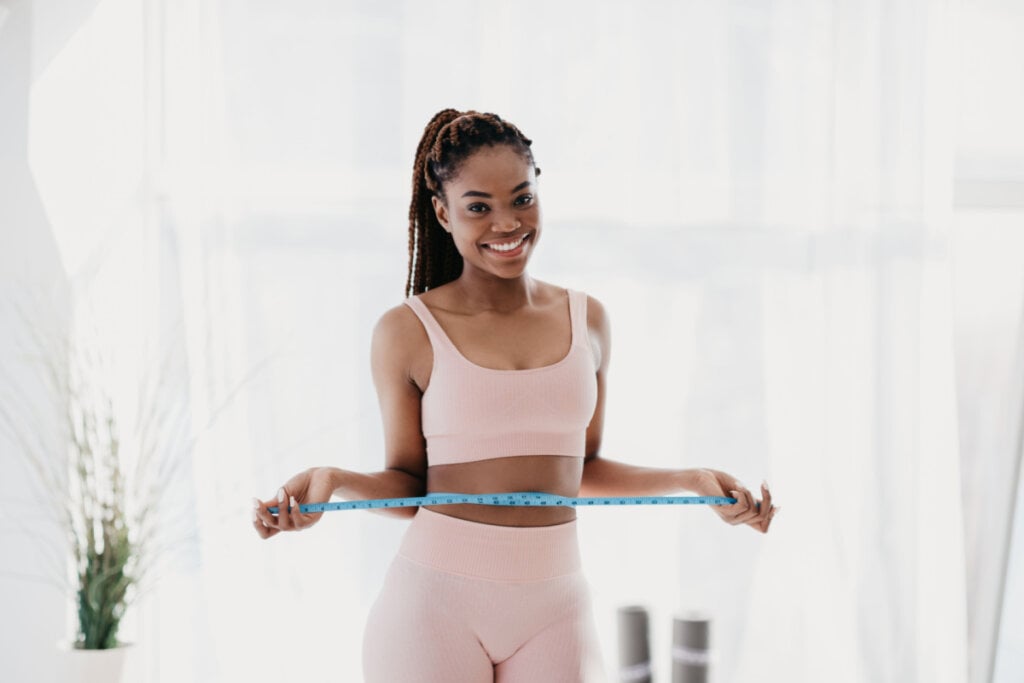 Mulher sorridente medindo cintura com fita métrica