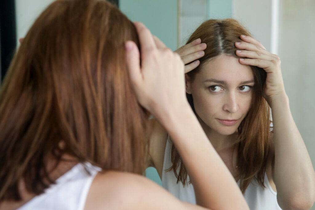 Mulher olhando o couro cabeludo em frente a um espelho 