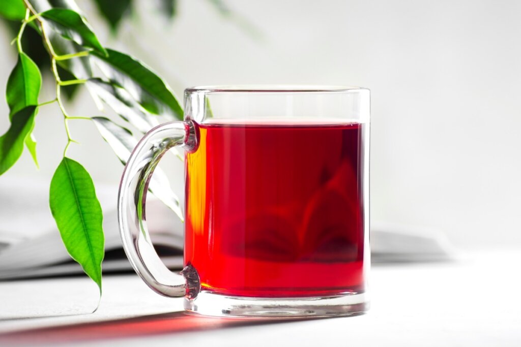 Xícara de vidro com chá vermelho em cima de uma mesa branca