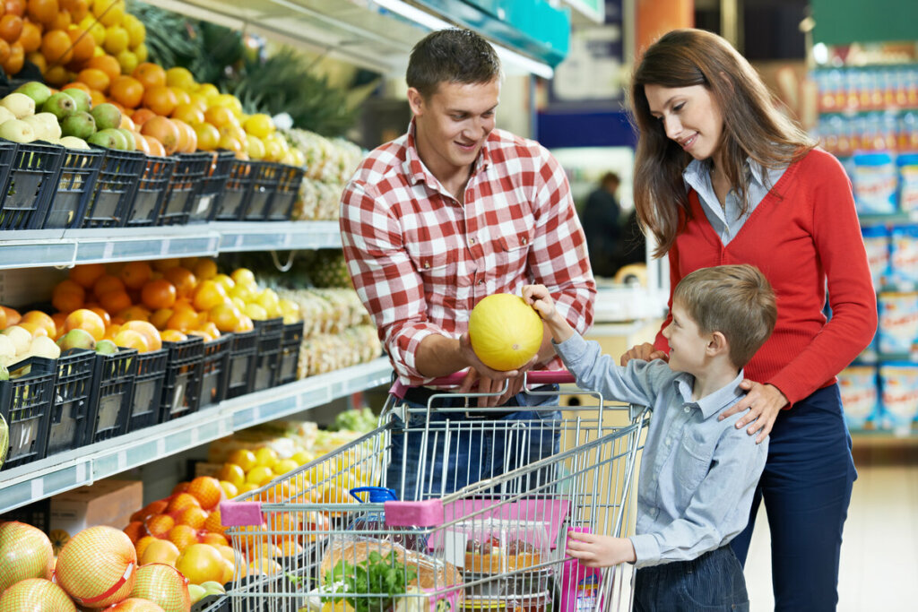 Homem, mulher e uma criança em um supermercado olhando um melão