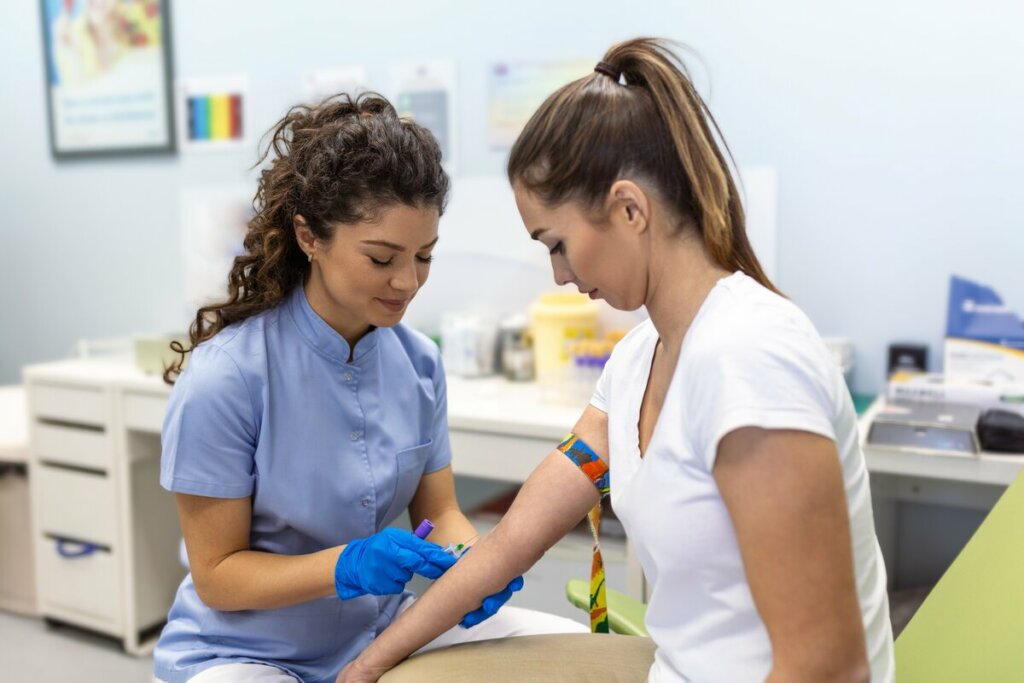 Mulher vestindo blusa branca sentada fazendo exame de sangue