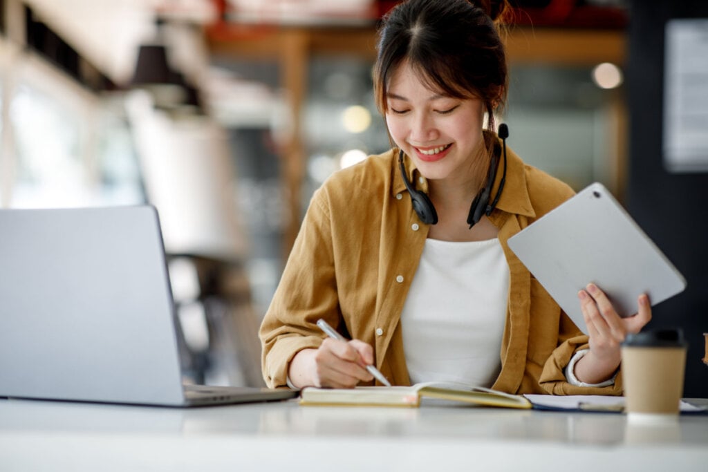 Mulher estudando com caderno, computador e tablet.