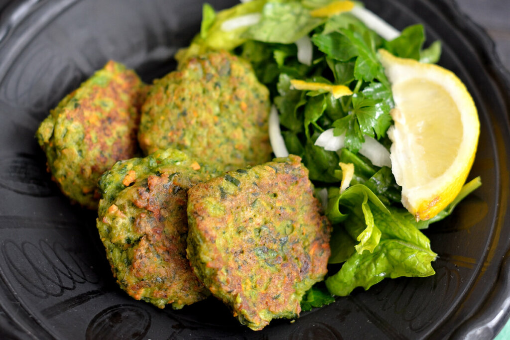 Hamburgueres de espinafre empilhados em cima de um prato preto com salada e rodelas de limão