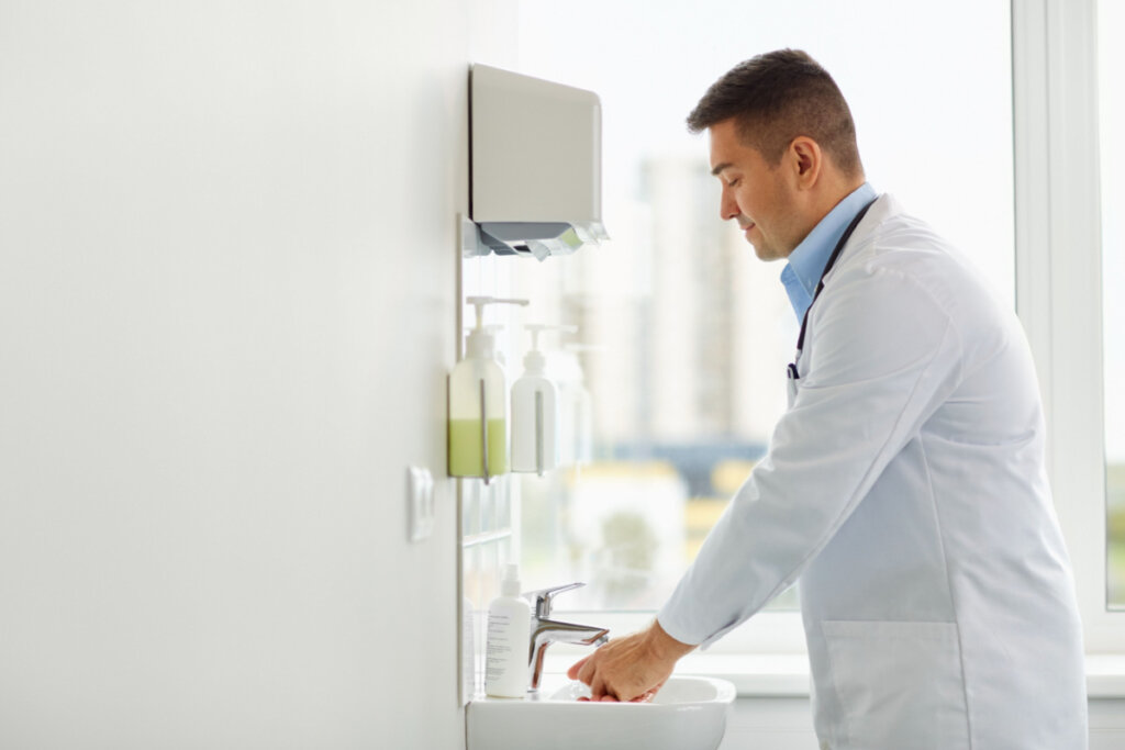 Médico com jaleco branco lavando as mãos em pia branca