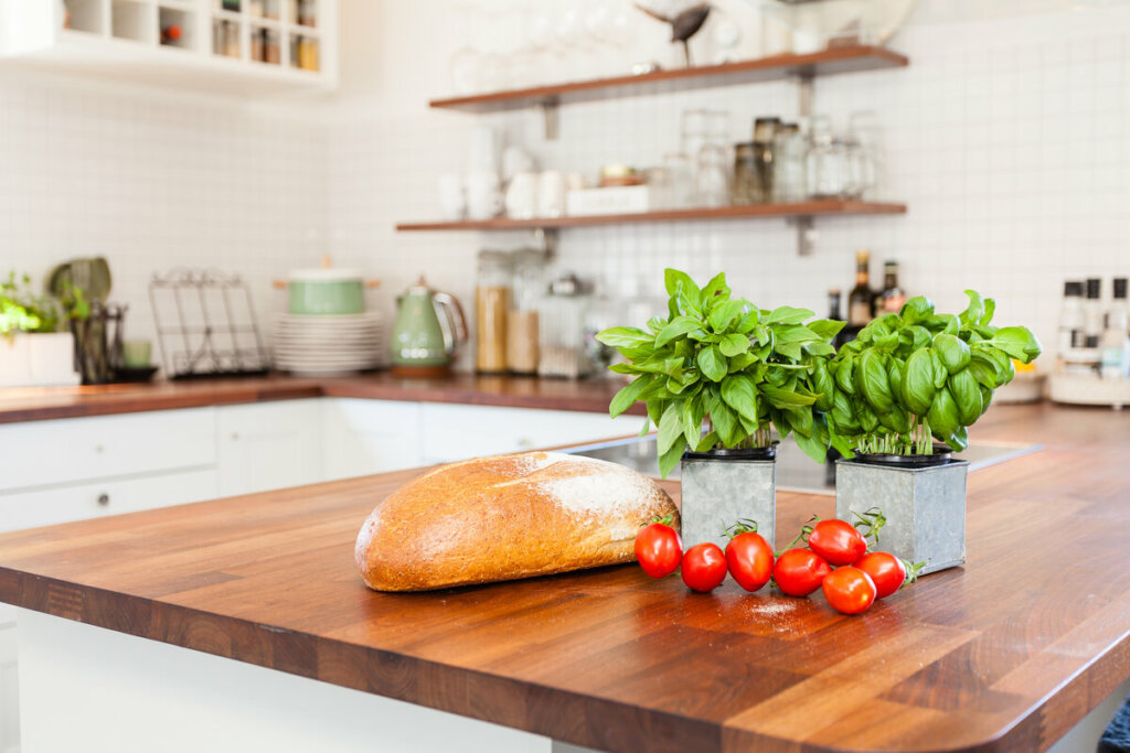 Cozinha com prateleiras e bancada de madeira com pães, tomate e vasos com manjericão 