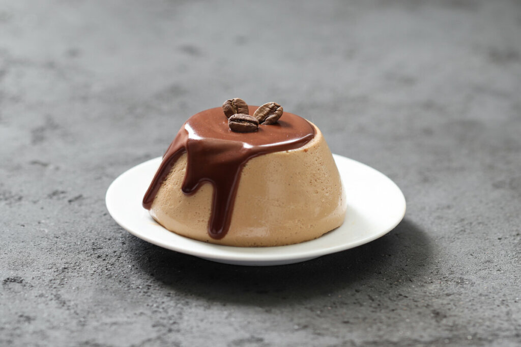 Panna cotta em cima de um prato branco decorada com calda de chocolare e grãos de café