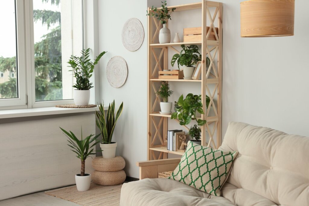 Sala de estar com sofá bege, almofada verde e branca e plantas espalhadas pelo ambiente