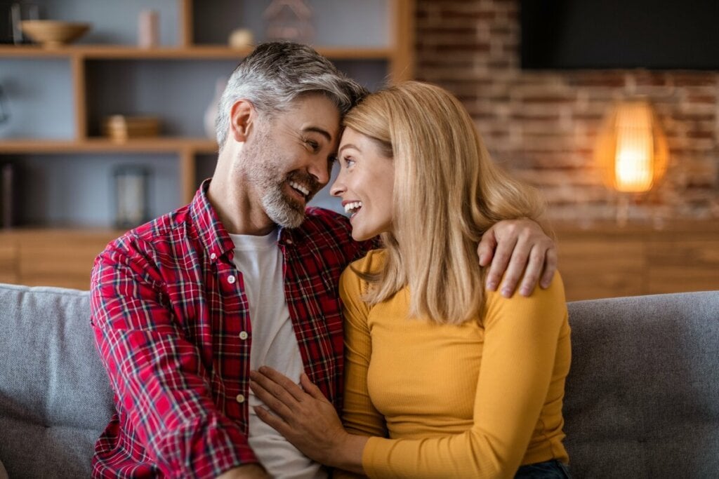 Homem e mulher sentados sorrindo e com as testas encostadas uma na outra