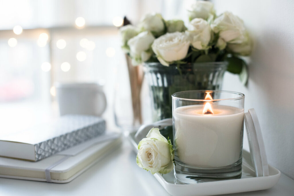 Rosas brancas em um vaso com vela branca ao lado e livros 