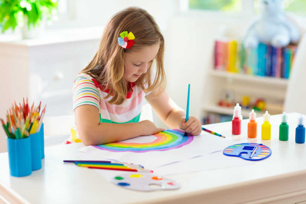 Menina sentada pintando um arco-íris em uma folha de papel 
