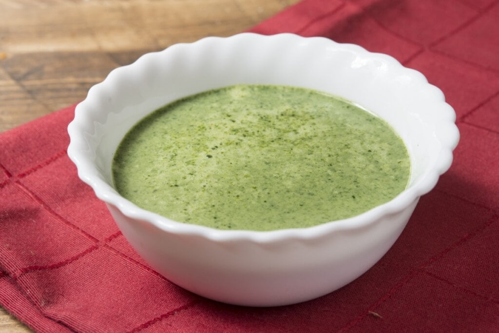 Recipiente branco com sopa de abacate em cima de uma mesa de madeira com pano vermelho