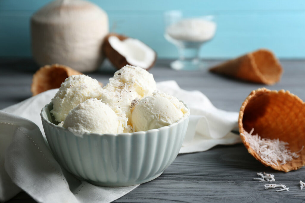 Recipiente branco com sorvete de coco em cima de uma mesa de madeira com casca de sorvete e pedaços de coco