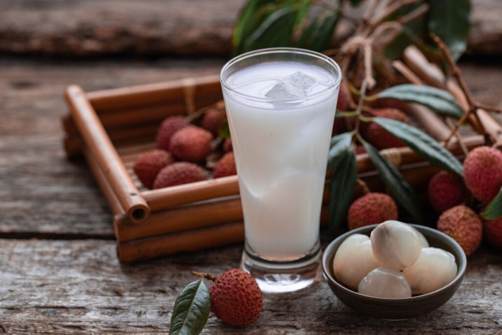 Copo de vidro com suco de lichia com gelo em cima de uma mesa de madeira