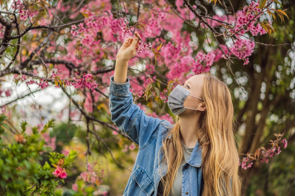 Mulher usando máscara e olhando uma árvore com flores rosas