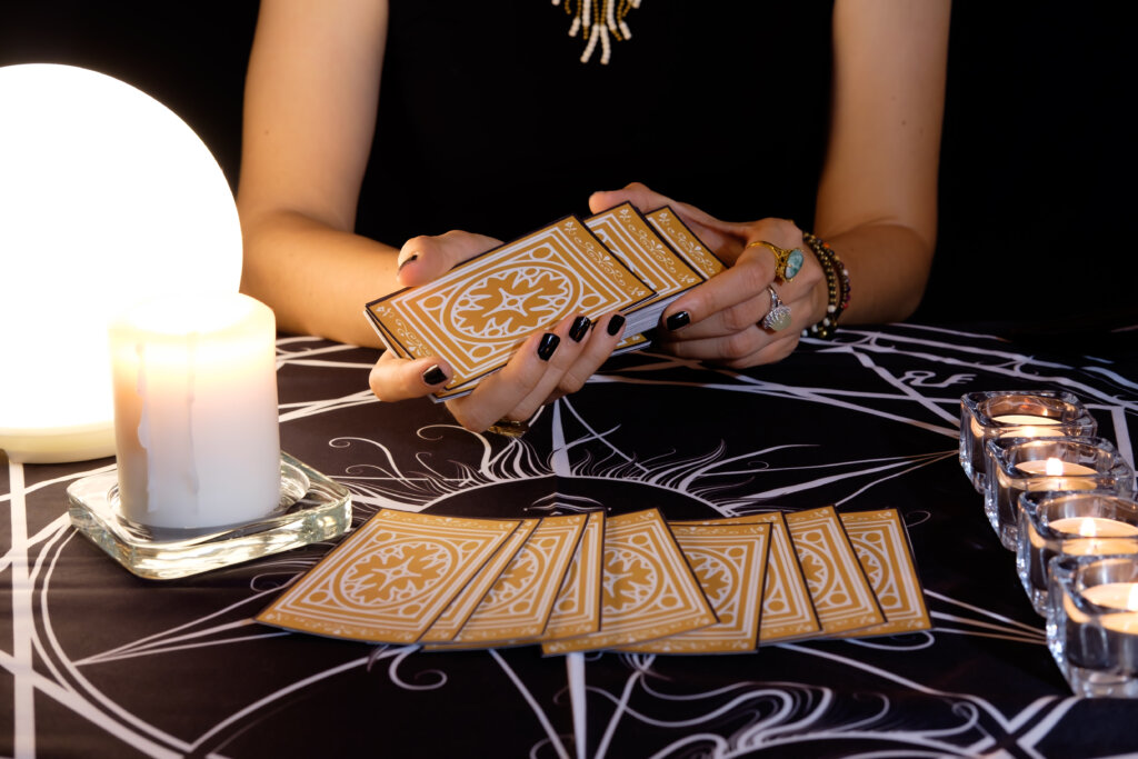 Cartomante embaralhando cartas; Cartas de tarô voltadas para baixo em uma mesa perto de uma bola de cristal e velas acesas