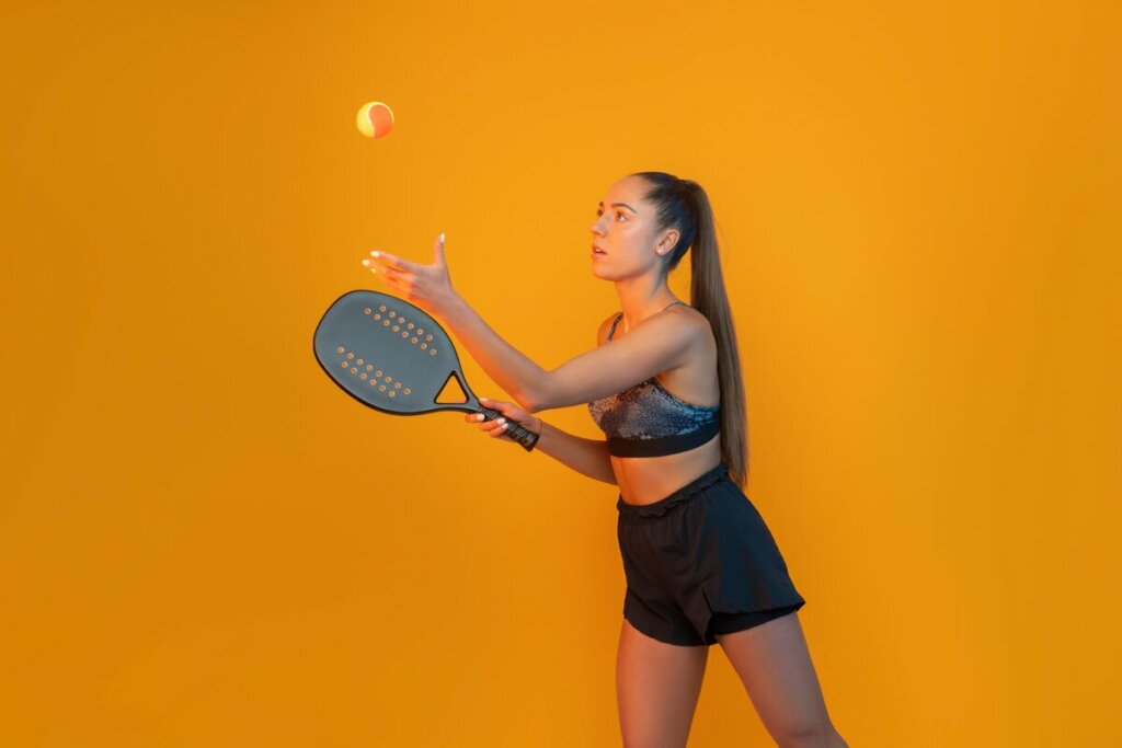 Mulher vestida com roupas leves e segurando uma raquete de beach tennis em um fundo amarelo