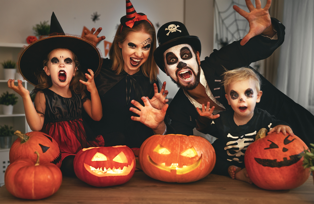 Duas crianças e dois adultos fantasiados de caveira, bruxa e pirata, com abóboras decorativas na frente deles