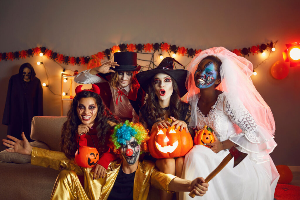 Jovens alegres vestidos de bruxa maluca, demônio, vampiro, noiva cadáver e palhaço com machado se divertindo juntos na festa de Halloween