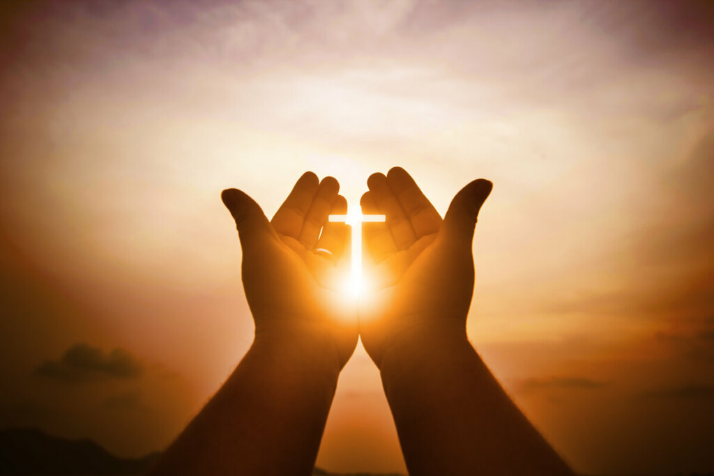 Mãos levantadas para o céu com os dedos formando uma cruz 