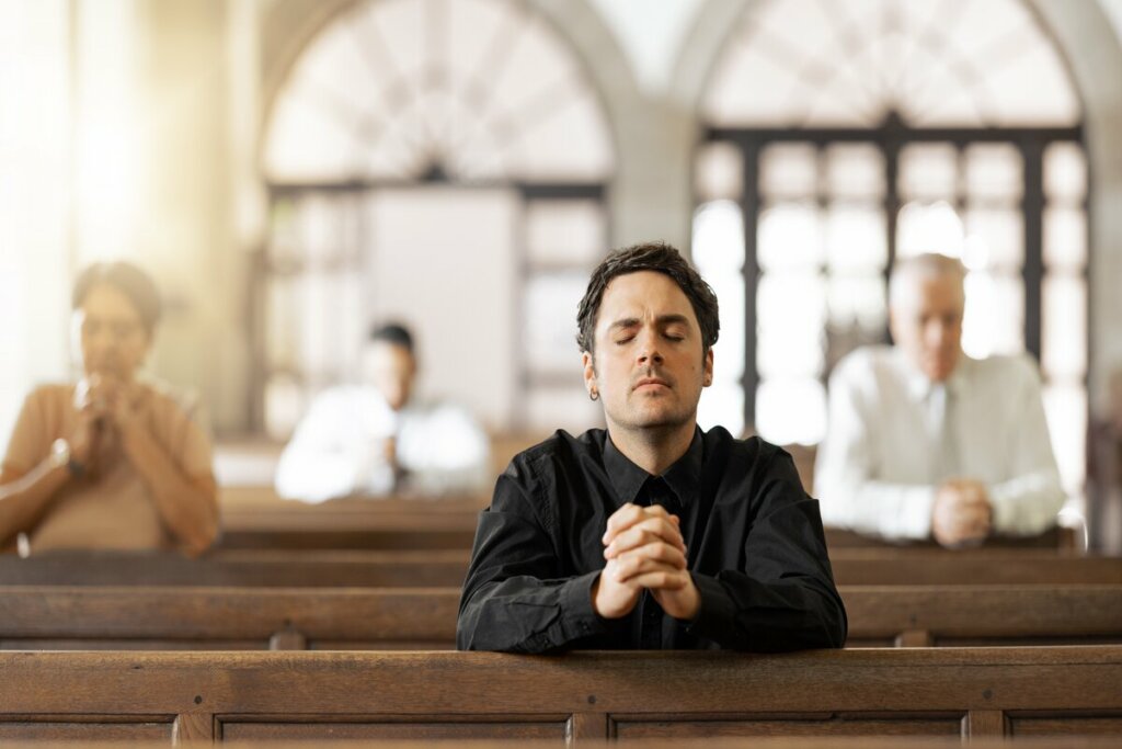 Homem vestindo roupa preta sentado em uma igreja orando 