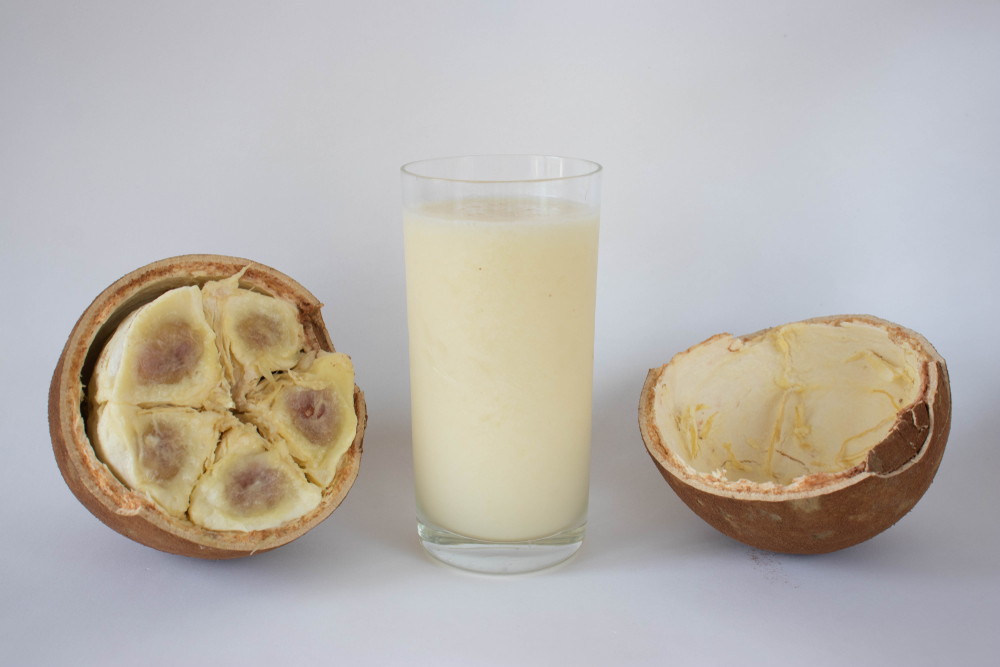 Um copo de suco de cupuaçu com a fruta cortada ao meio ao lado
