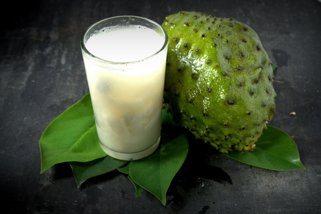 Um copo de suco de graviola com folhas frescas de graviola no fundo de madeira cinza