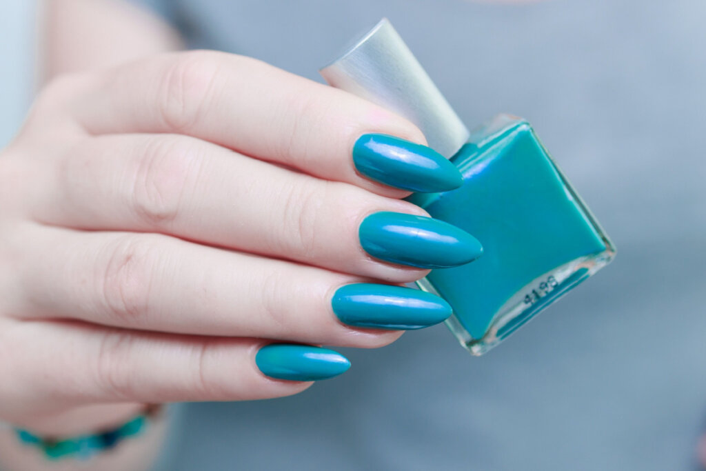 Mãos femininas com unhas na cor azul segurando um esmalte azul